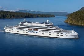 BC Ferries Island Class second-series hybrid road ferry sailing among forested British Columbia coastline.