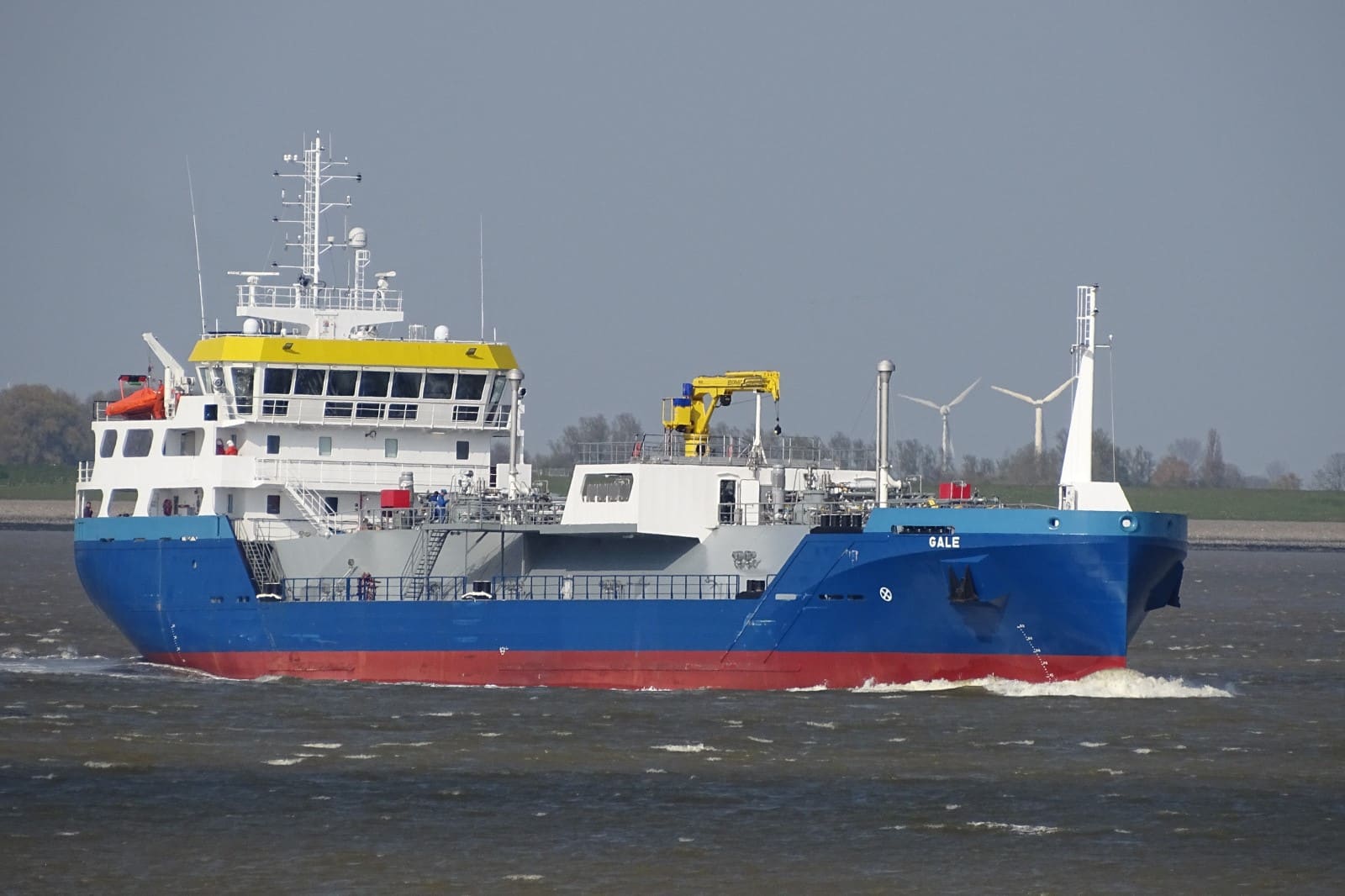 LPG tanker Gale for Chemgas underway on the Dutch river system, blue hull with yellow wheelhouse, wind turbines in the background.