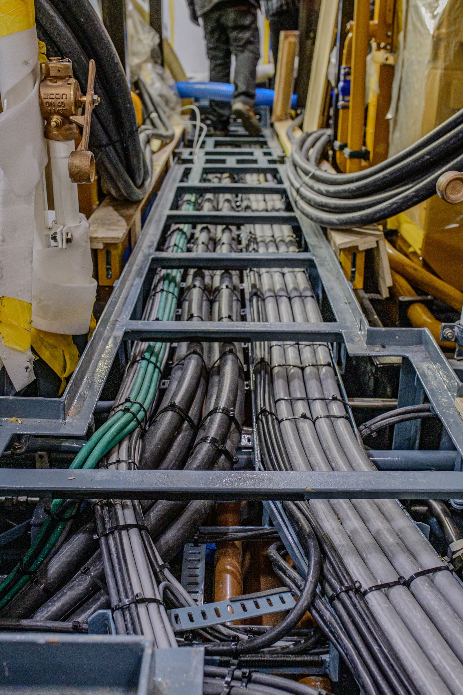 Vertical cable trunk with bundled marine cables routed along structural framing, technicians working at the far end