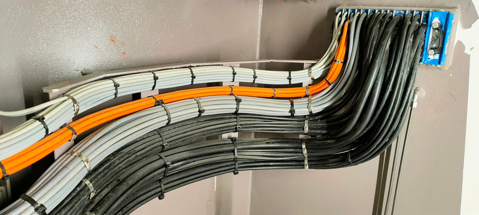 Wall-mounted cable run with grey and orange marine cables turning at a 45-degree angle along structural supports