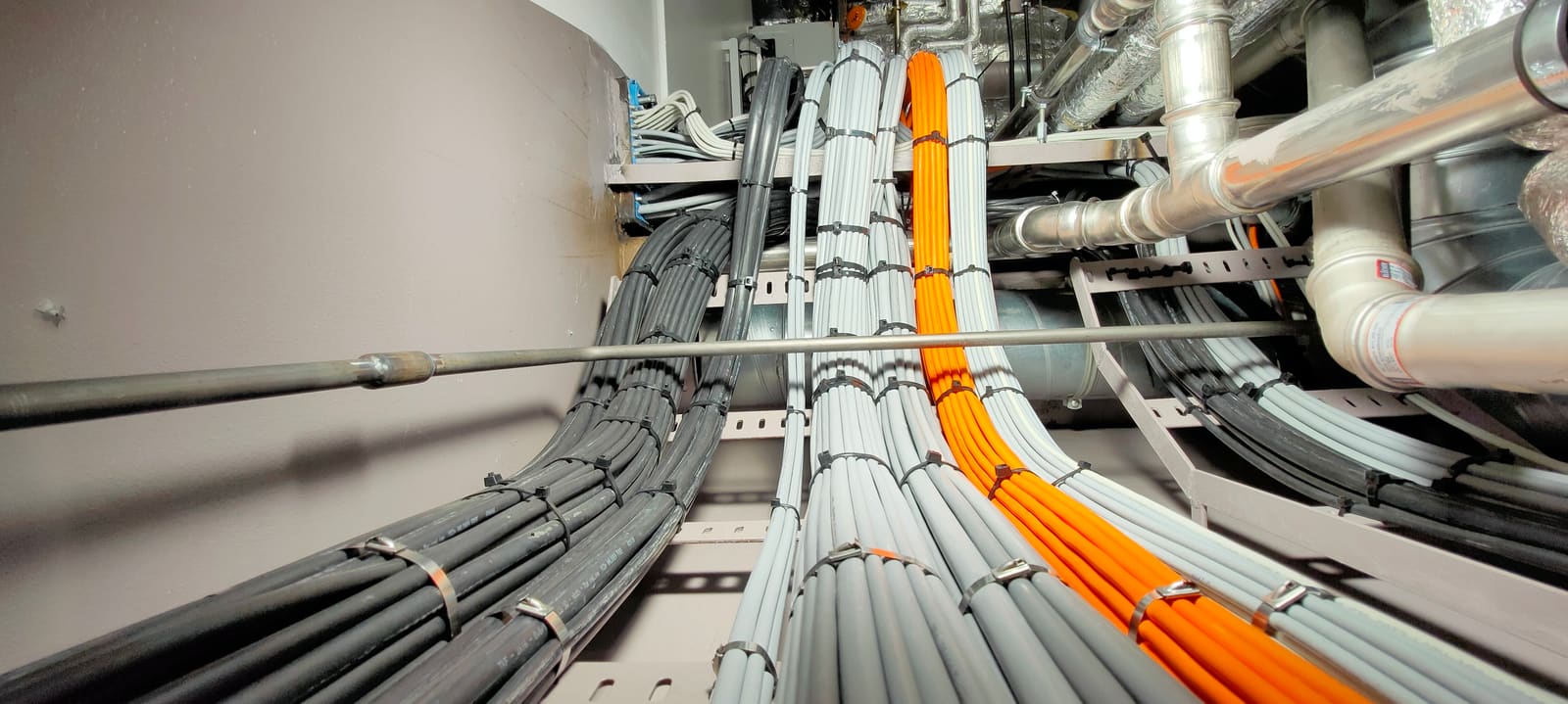 Multi-tier cable routing through a vessel compartment with grey, orange and black bundles converging on a central junction