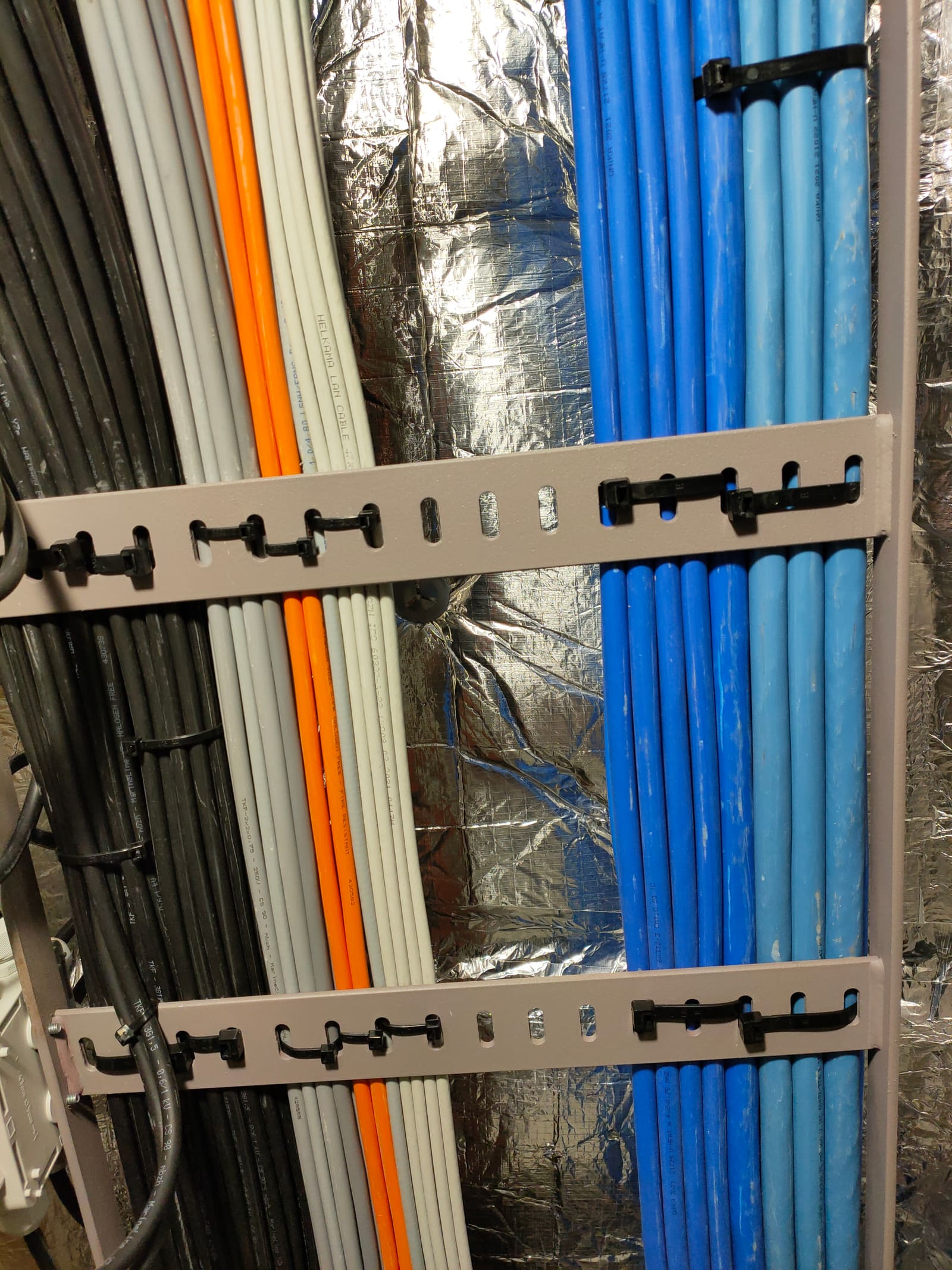 Vertical cable supports with grey, orange and blue marine cables routed in parallel along an insulated bulkhead