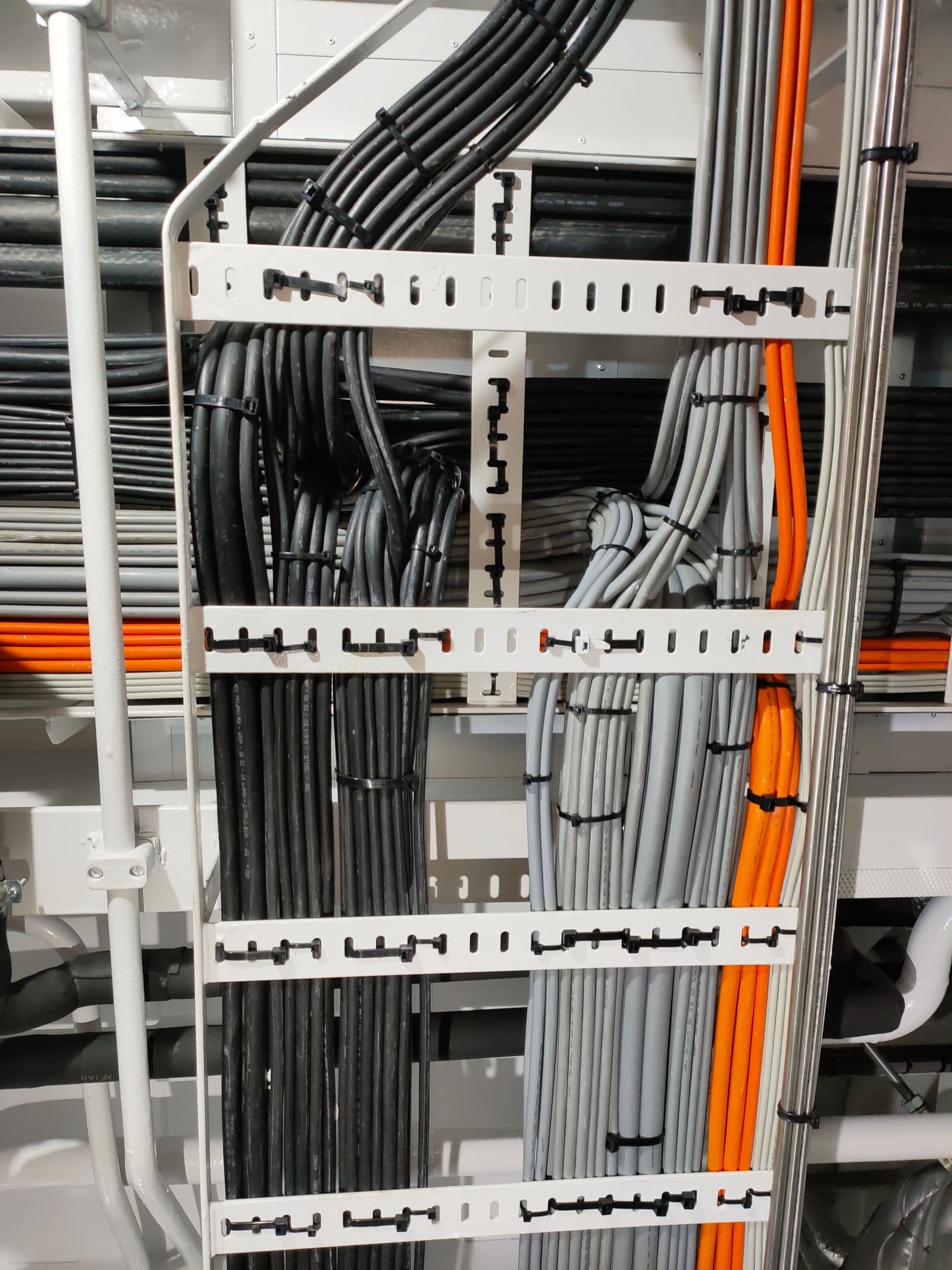 Multi-level horizontal cable tray rack with grey and orange marine cables running parallel along a bulkhead
