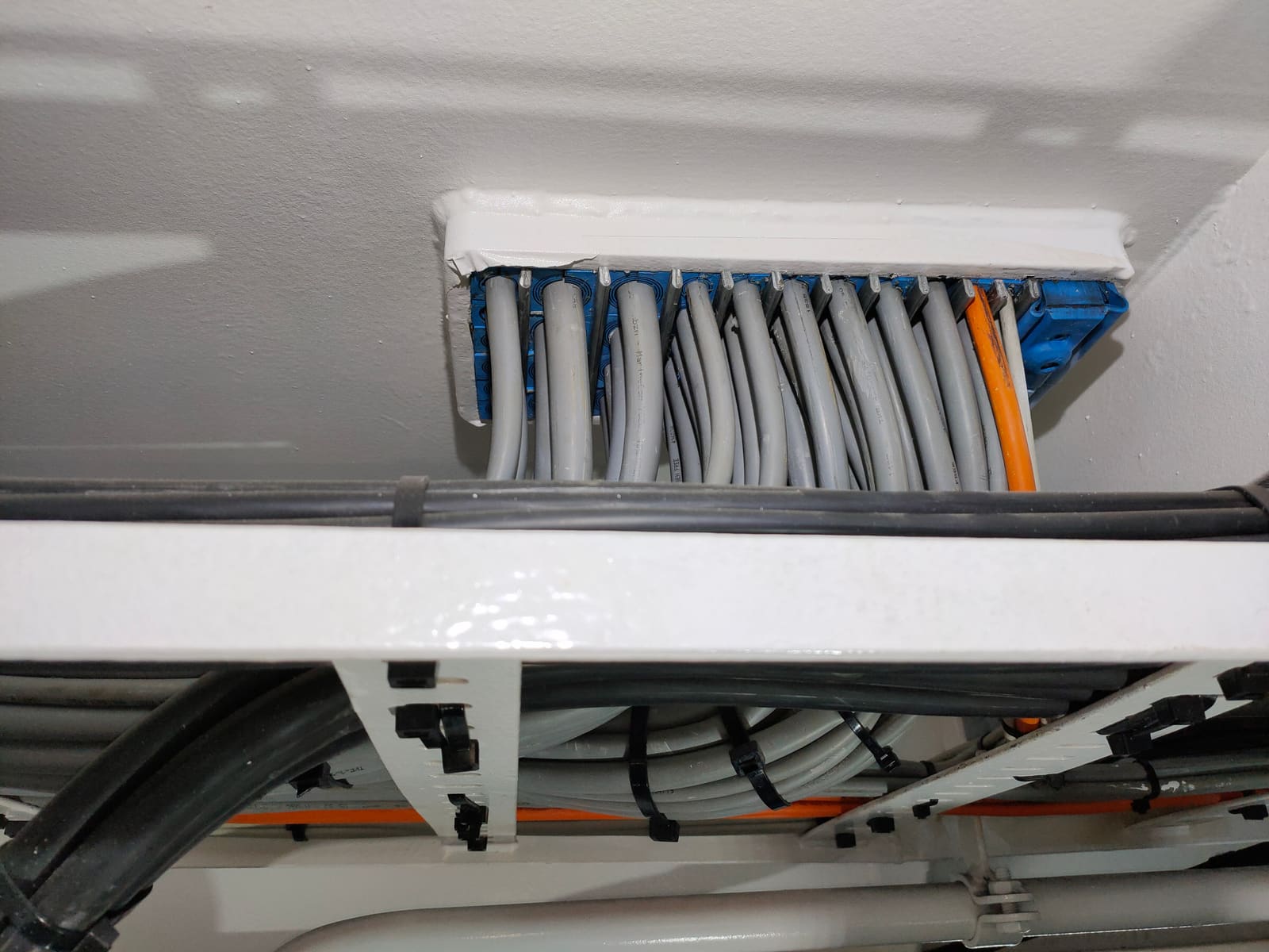 Cabinet entry cable tray penetrating a thermal insulation strip with grey and orange marine cables continuing through