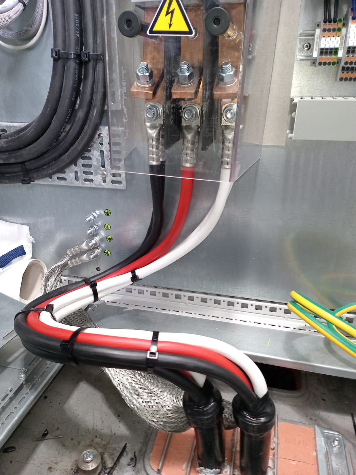Black, red and white marine power cables terminated to a transformer's primary studs through compression lugs under a high-voltage warning label