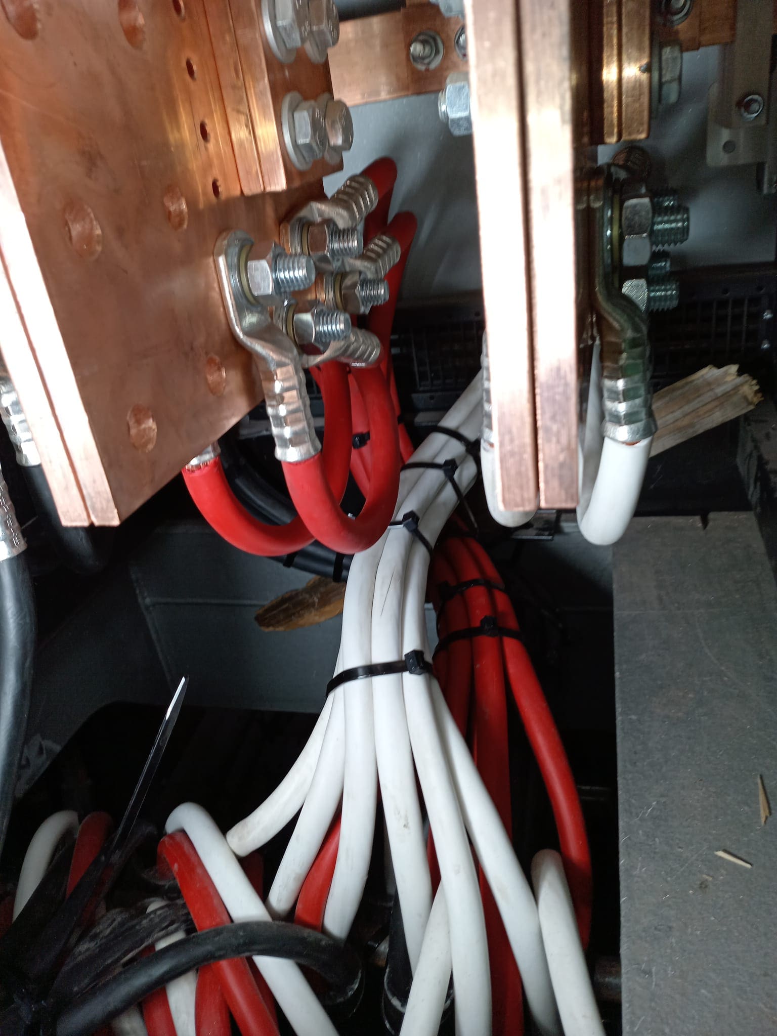 Switchboard busbar termination detail with red and white single-core cables bolted to copper buses through compression lugs