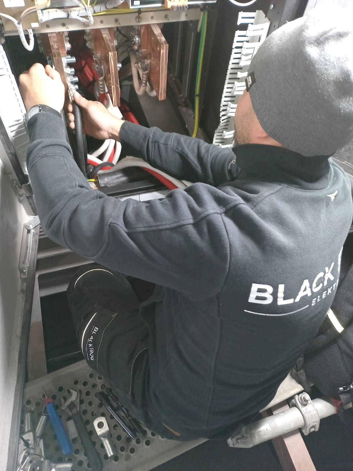Black Frog Elektro technician in branded hoodie working inside a marine switchboard cabinet to terminate power cables onto busbars