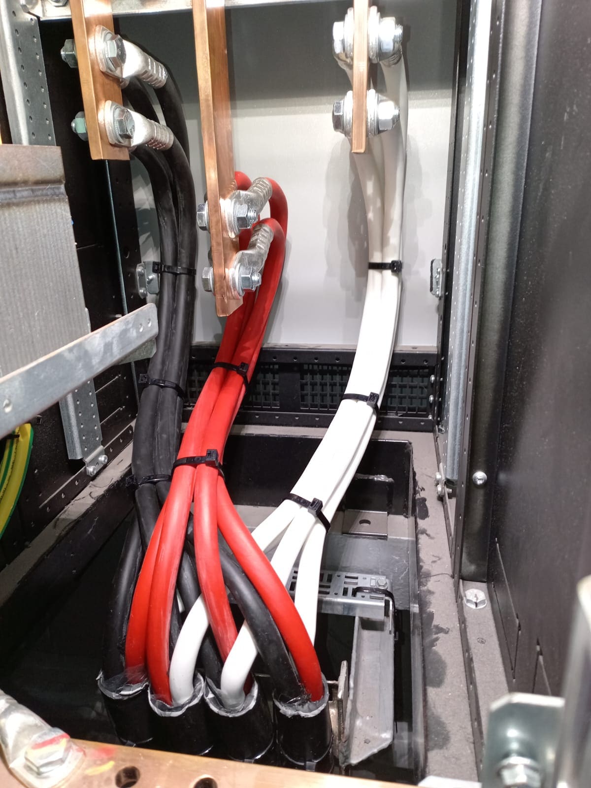 Distribution panel busbar bay with paired black, red and white cables terminated to copper bus stabs through compression lugs