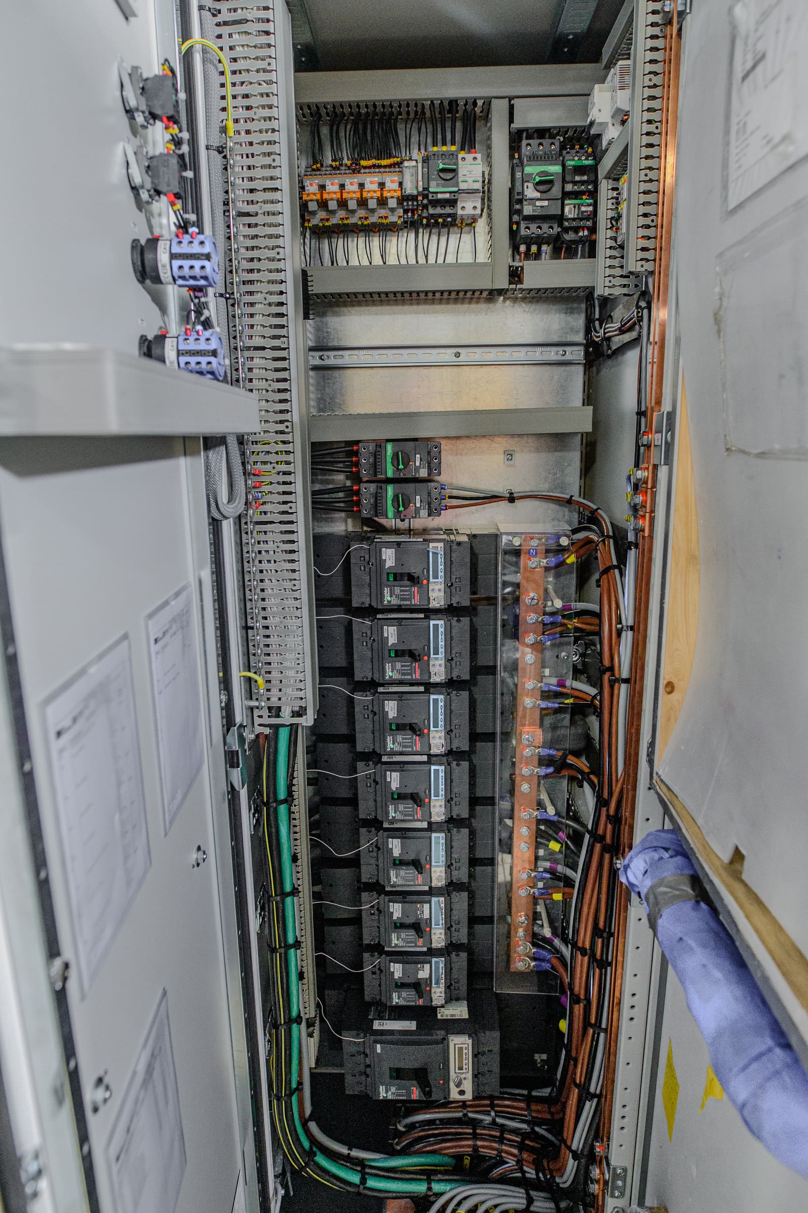 Inside view of a low-voltage motor control cabinet with column of moulded-case circuit breakers fed by copper bus and outgoing cables