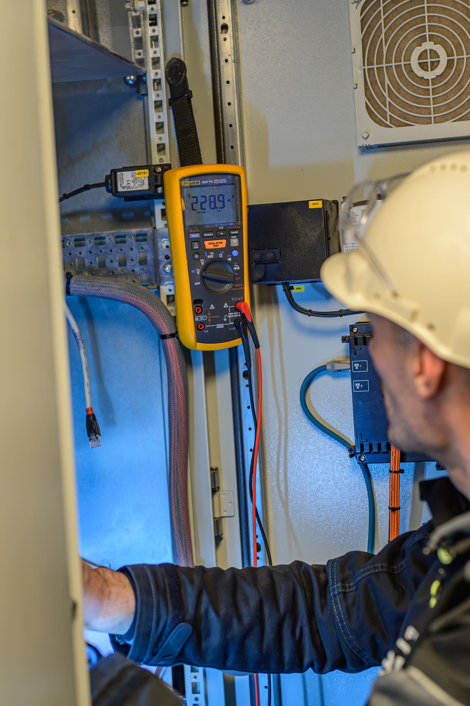 Marine commissioning engineer measuring 230 V AC bus voltage on a low-voltage cabinet with a Fluke multimeter during cold wire testing