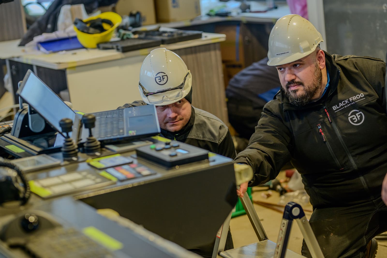 Two Black Frog Elektro commissioning engineers in branded jackets verifying joystick controls on a vessel bridge during sea trials