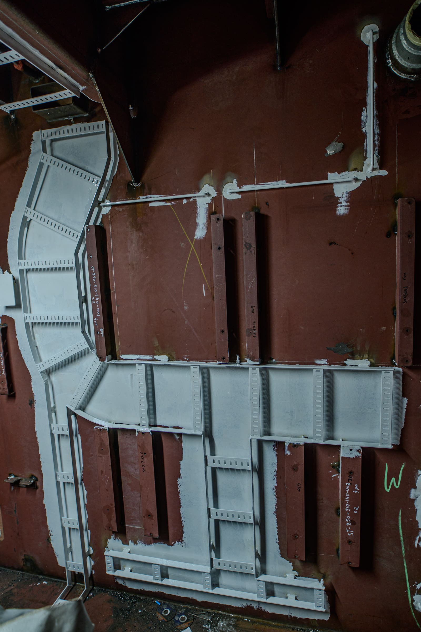 White-painted cable tray ironwork installed on a vessel's red bulkhead with intersecting cable routes ready for installation