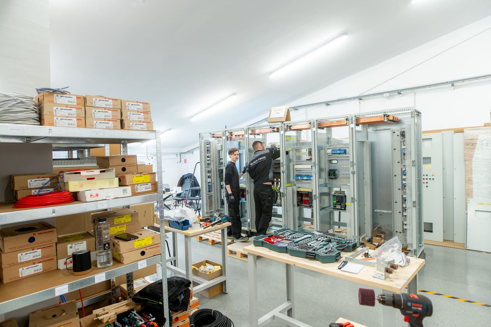 Wide view of the Black Frog Elektro panel-building workshop with technicians wiring a marine switchgear bay