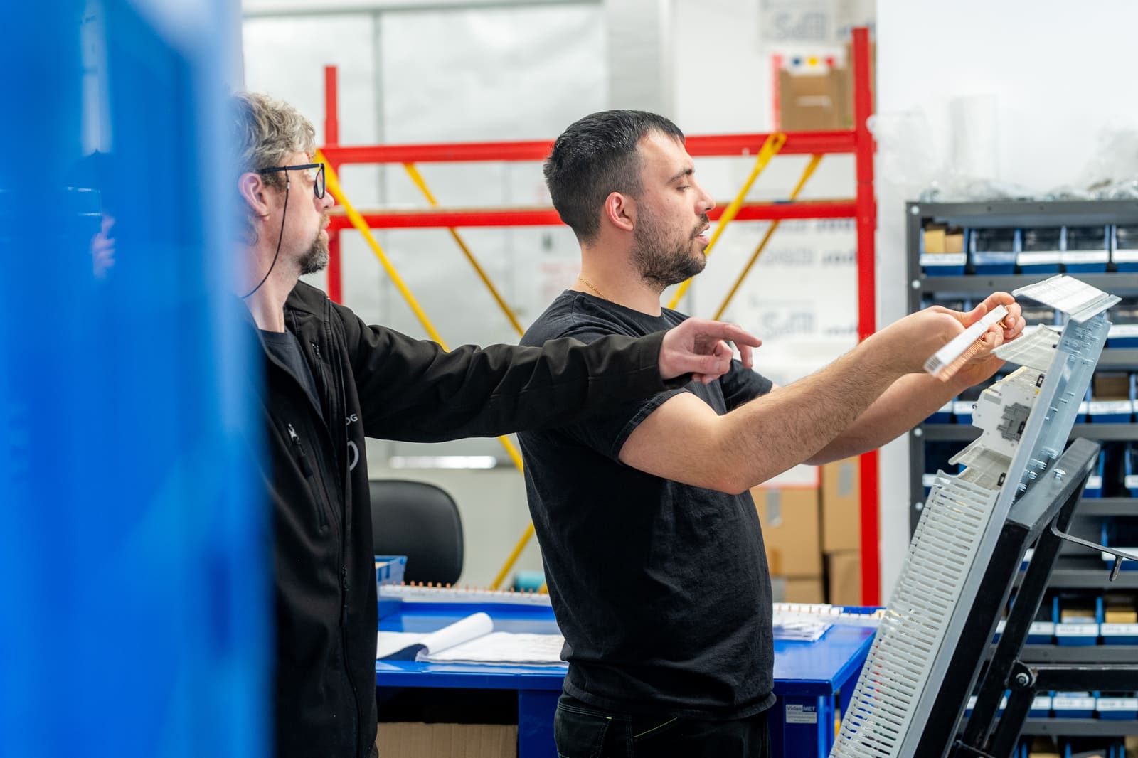 Two Black Frog Elektro panel builders cross-checking a wiring loom against a build sheet at a workbench in the workshop