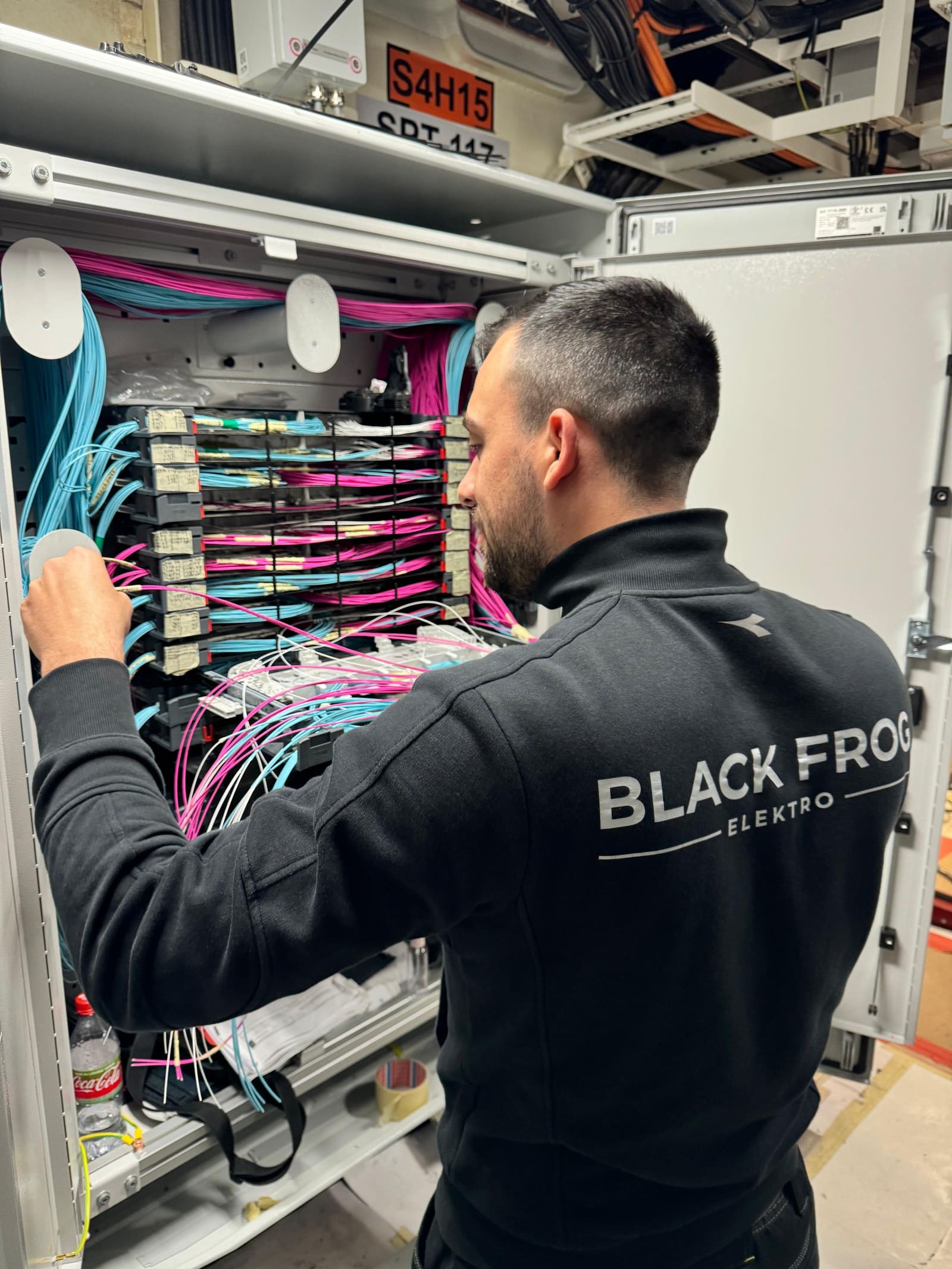 Black Frog Elektro technician terminating magenta and aqua fiber optic patch cords inside an open marine fiber optic distribution cabinet.
