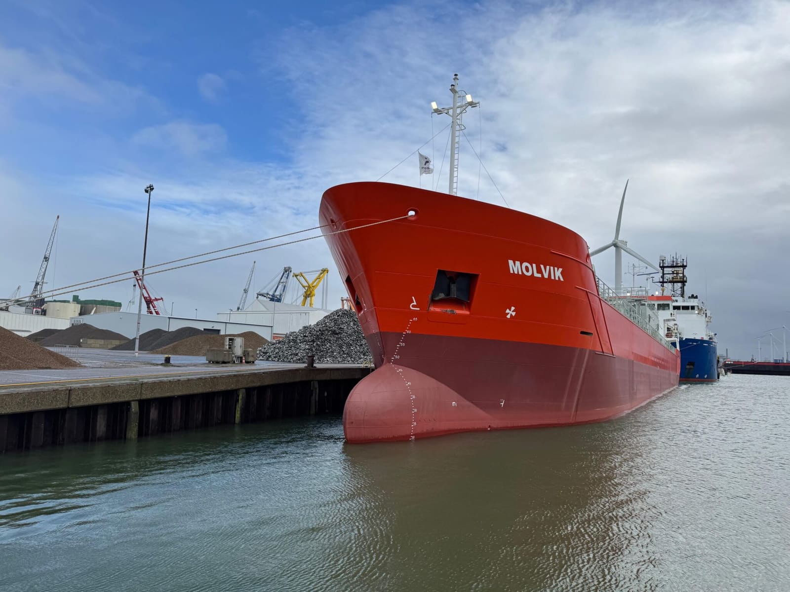 Cement carrier Molvik for SMT Shipping at port quay with cranes and wind turbine in the background.